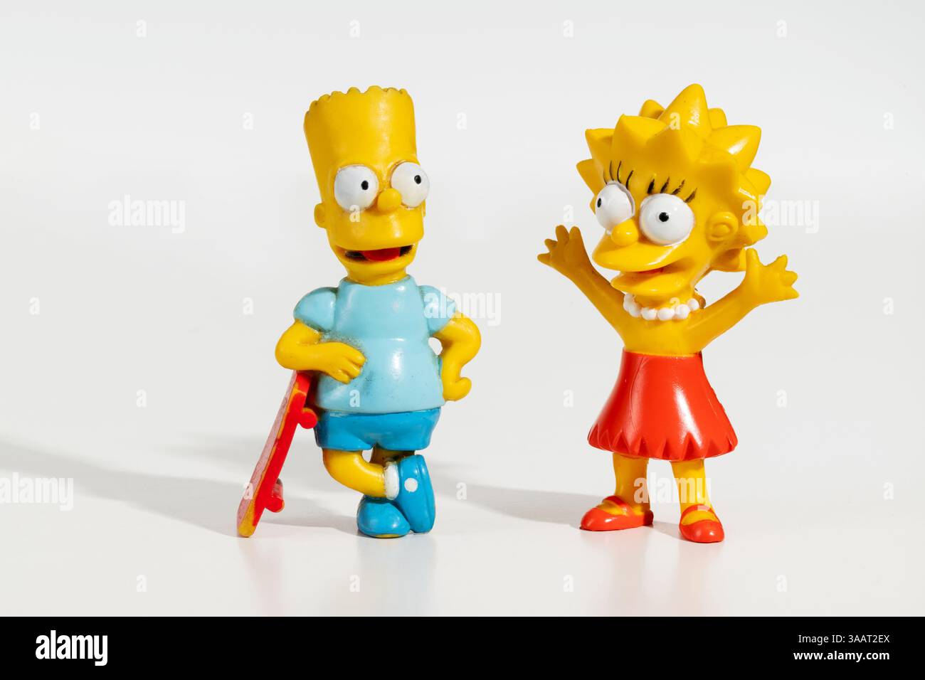 Bart Simpson lehnt sich auf Skateboard und Lisa Simpson mit erhobenen Armen, zwei Figuren auf weißem Hintergrund Stockfoto