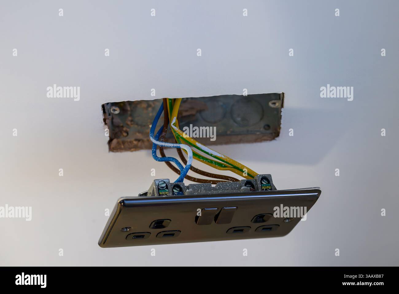 Freiliegende Wandsteckdose mit sichtbarer Verkabelung während der elektrischen Installation – ideal für Renovierungen, Heimwerkerarbeit, Sicherheitsbewusstsein oder Visualisierungen elektrischer Systeme Stockfoto