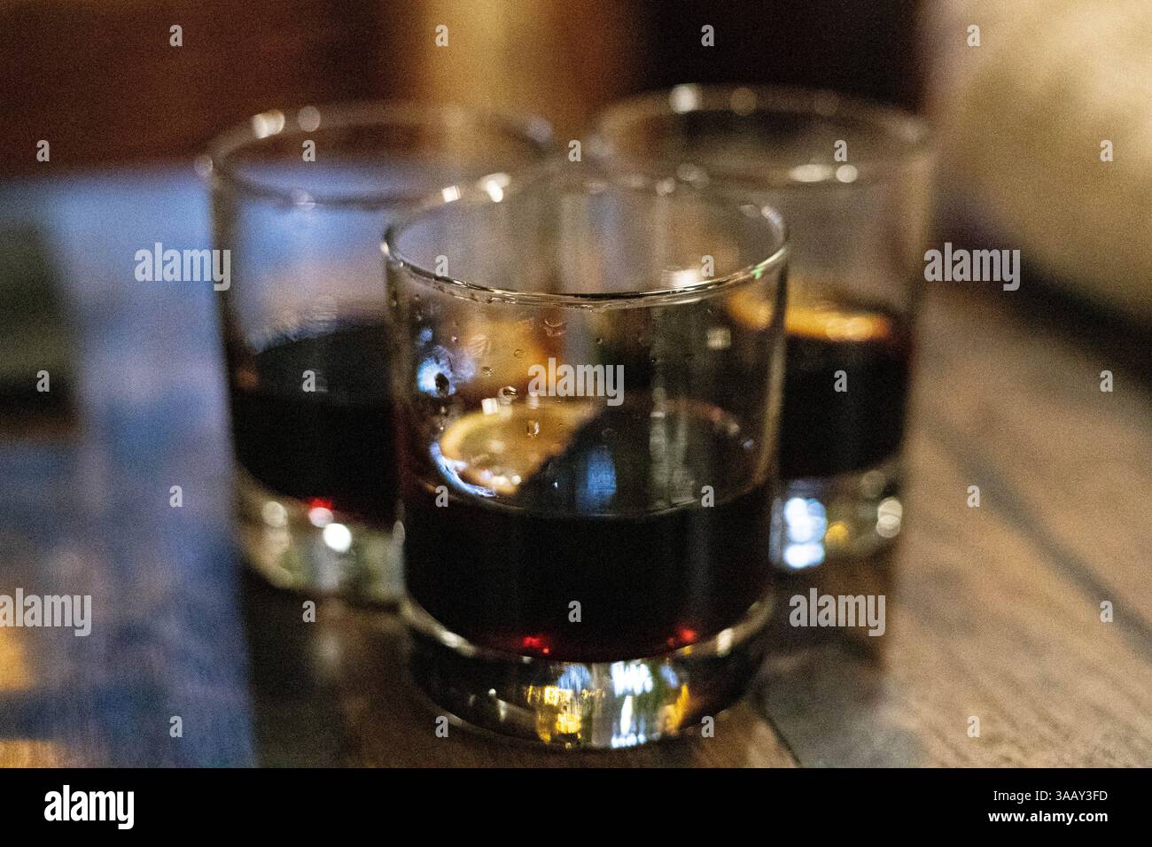 Drei Freunde feiern einen Geburtstag, indem sie drei Gläser alkoholischer Getränke mit Kirschen in einem Club im gestreuten Licht anschlagen Stockfoto