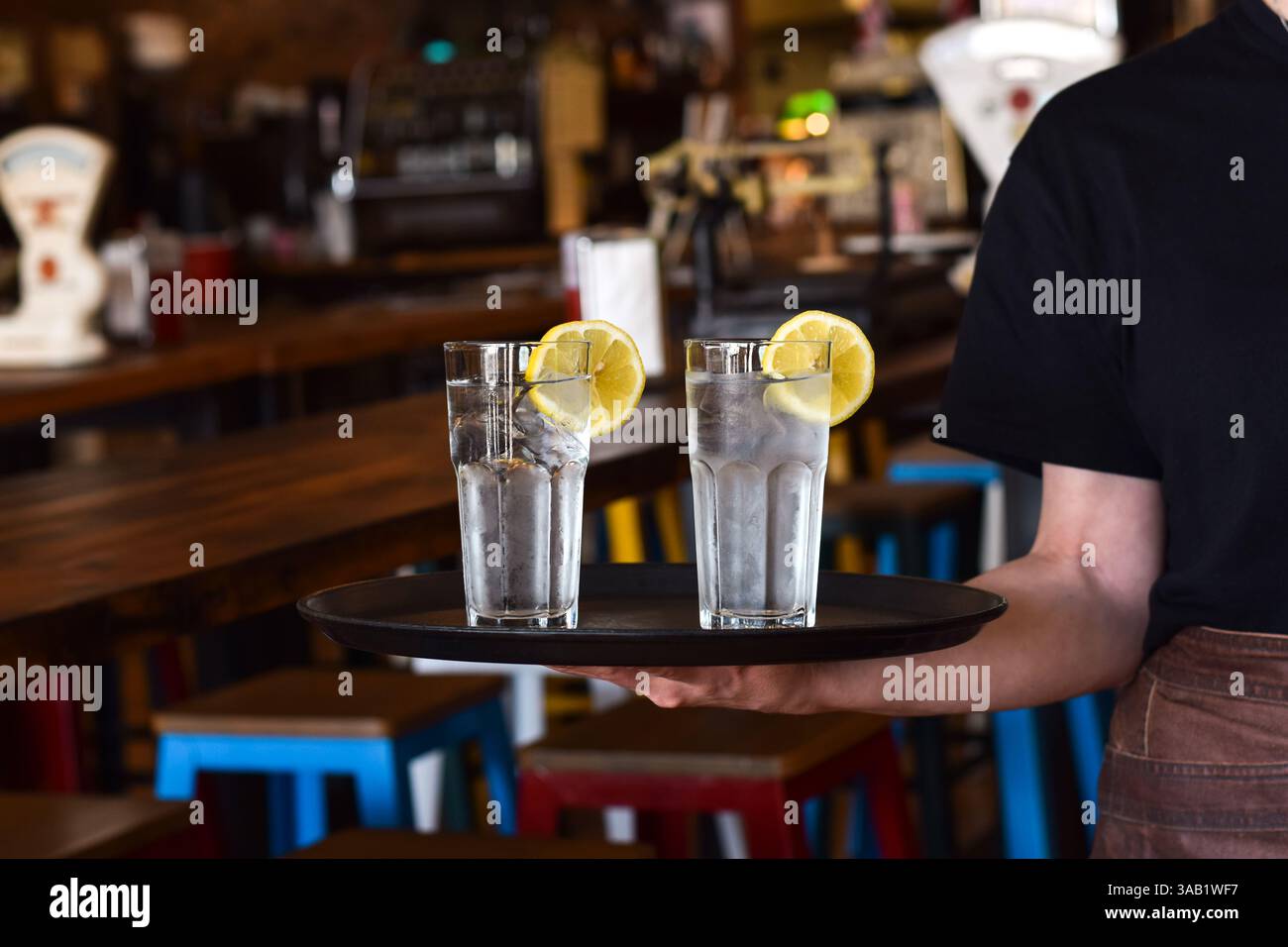 Der Kellner im Restaurant hält ein Tablett mit zwei Gläsern mit kaltem Wasser, Eis und Zitronenscheibe Stockfoto