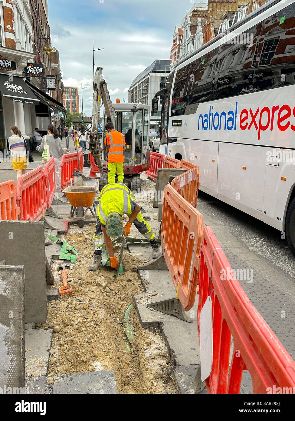 London, England, Großbritannien - 27. Juni 2023: Mann, der einen Graben auf einem Bürgersteig im Zentrum von London aushebt, während der Verkehr auf der anderen Seite der Sicherheitsbarriere vorbeifährt Stockfoto