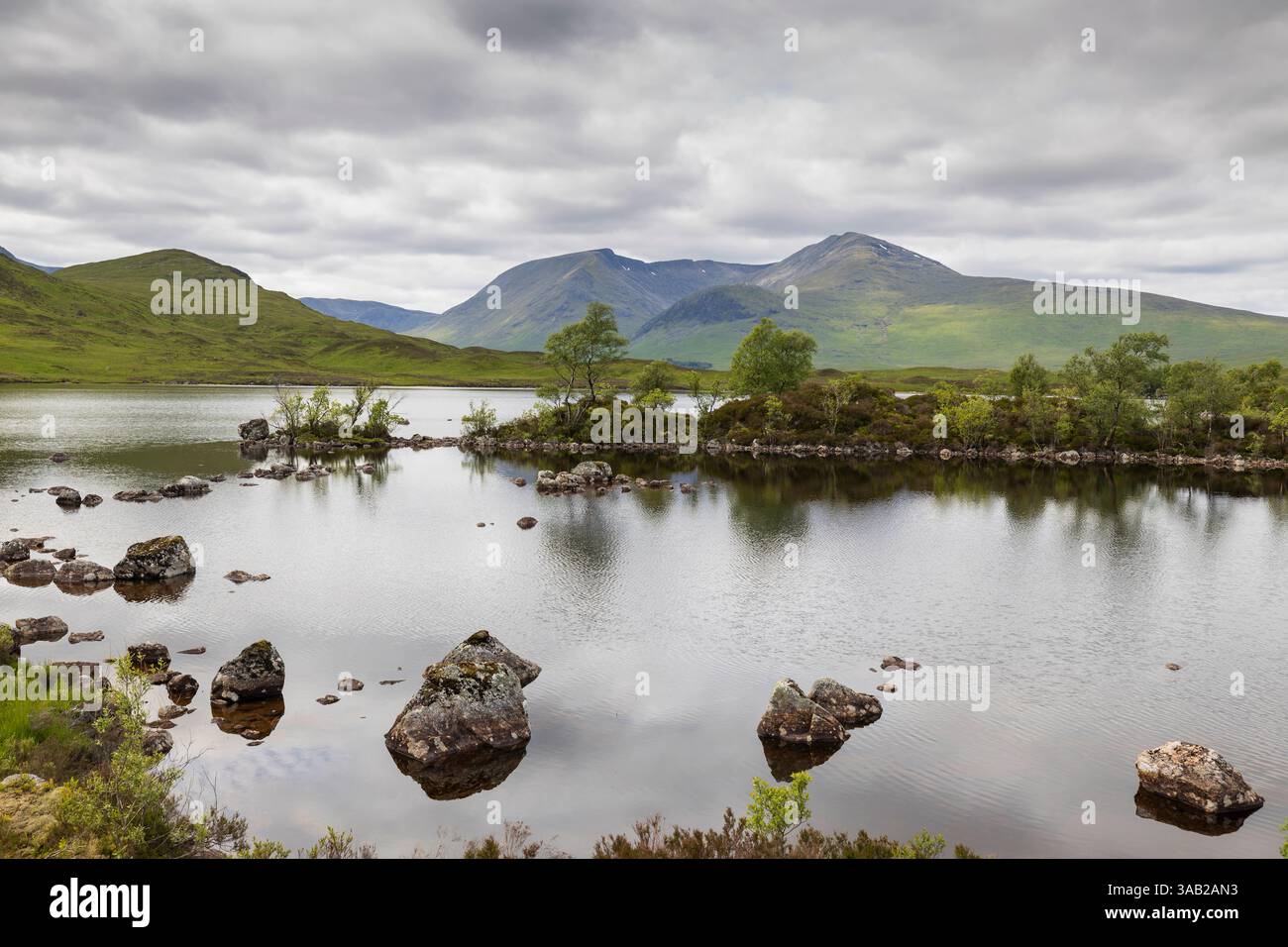 loch im schottischen Tiefland mit Felsblöcken und Bäumen mit niedrigen Wolken reflektiert Stockfoto