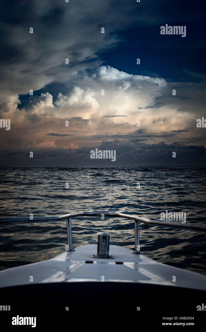 Eine filmische Perspektive aus dem Bug eines Bootes mit Blick auf das offene Wasser unter dramatischen Sturmwolken, was auf einen bevorstehenden Wetterwechsel hindeutet Stockfoto