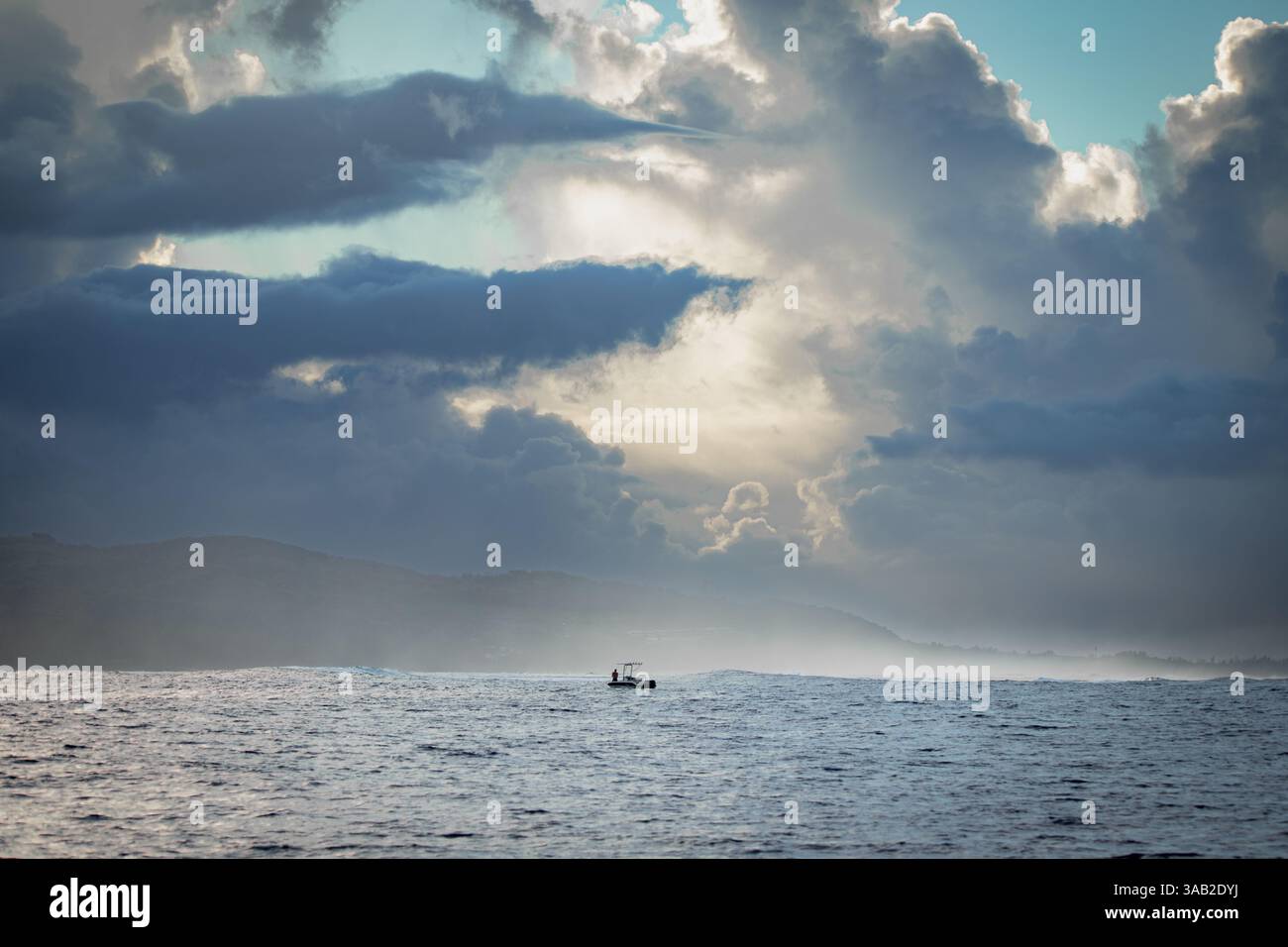 Ein einsames Fischerboot schwimmt auf dem Ozean unter den gewaltigen, dramatischen Wolken nahe der Küste von Mauritius, mit stimmungsvoller Beleuchtung und atmosphärischer Tiefe. Stockfoto