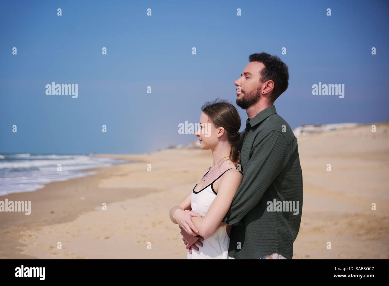 Romantisches Paar genießt eine friedliche Umarmung an einem breiten, leeren Strand, die Meeresbrise und die ruhige Aussicht auf die Küste genießen. Stockfoto