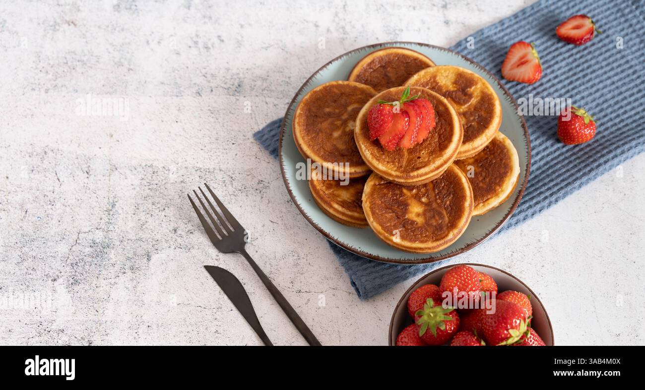 Hausgemachter Pfannkuchenstapel mit Heidelbeeren, Himbeeren und Erdbeeren auf einem weißen Teller mit einem blauen Tuch auf einer hellgrauen Tischplatte Stockfoto