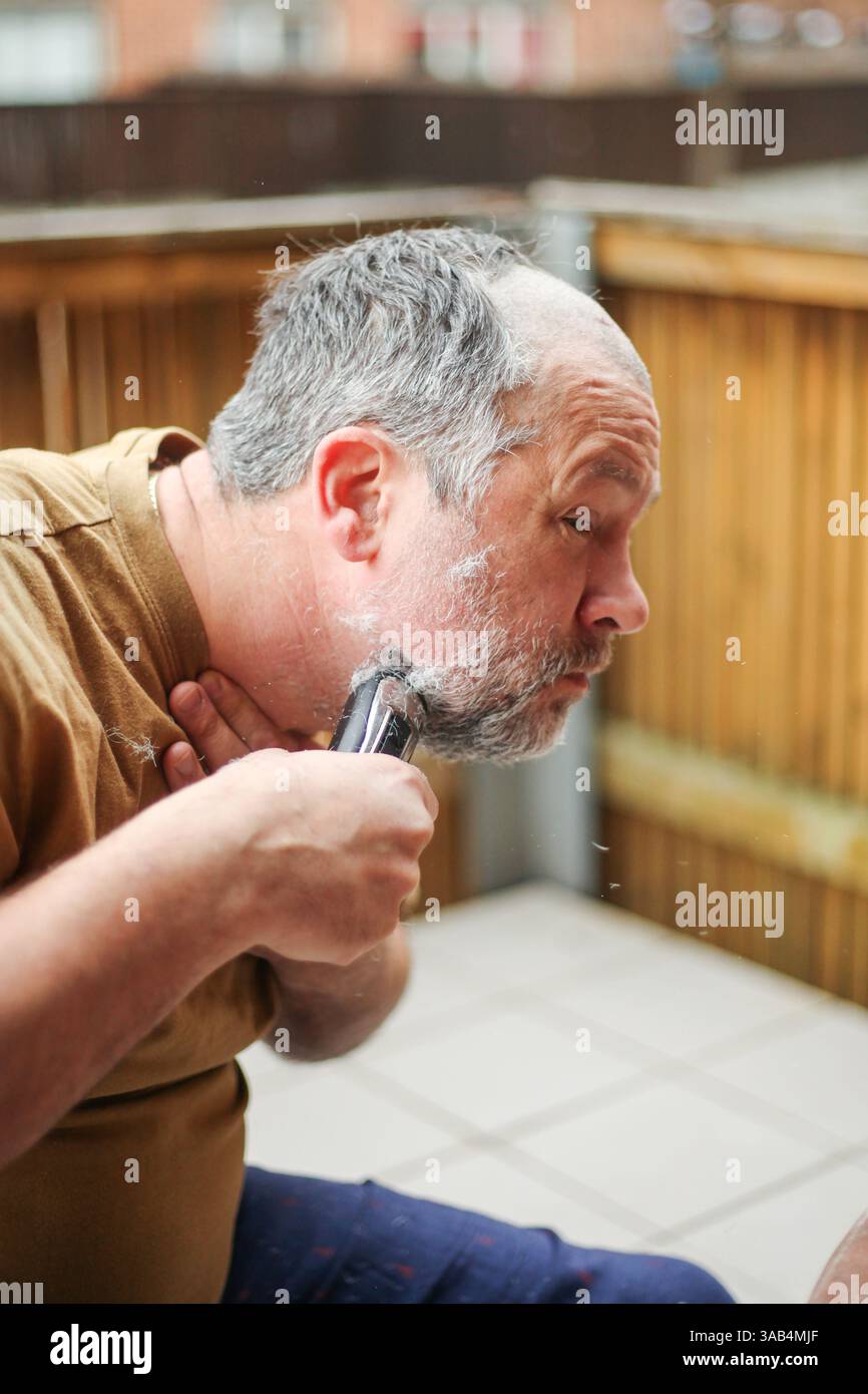 Älterer Mann rasiert sich auf einer Terrasse, Gesichtsausdruck zeigt Konzentration und Sorgfalt Stockfoto