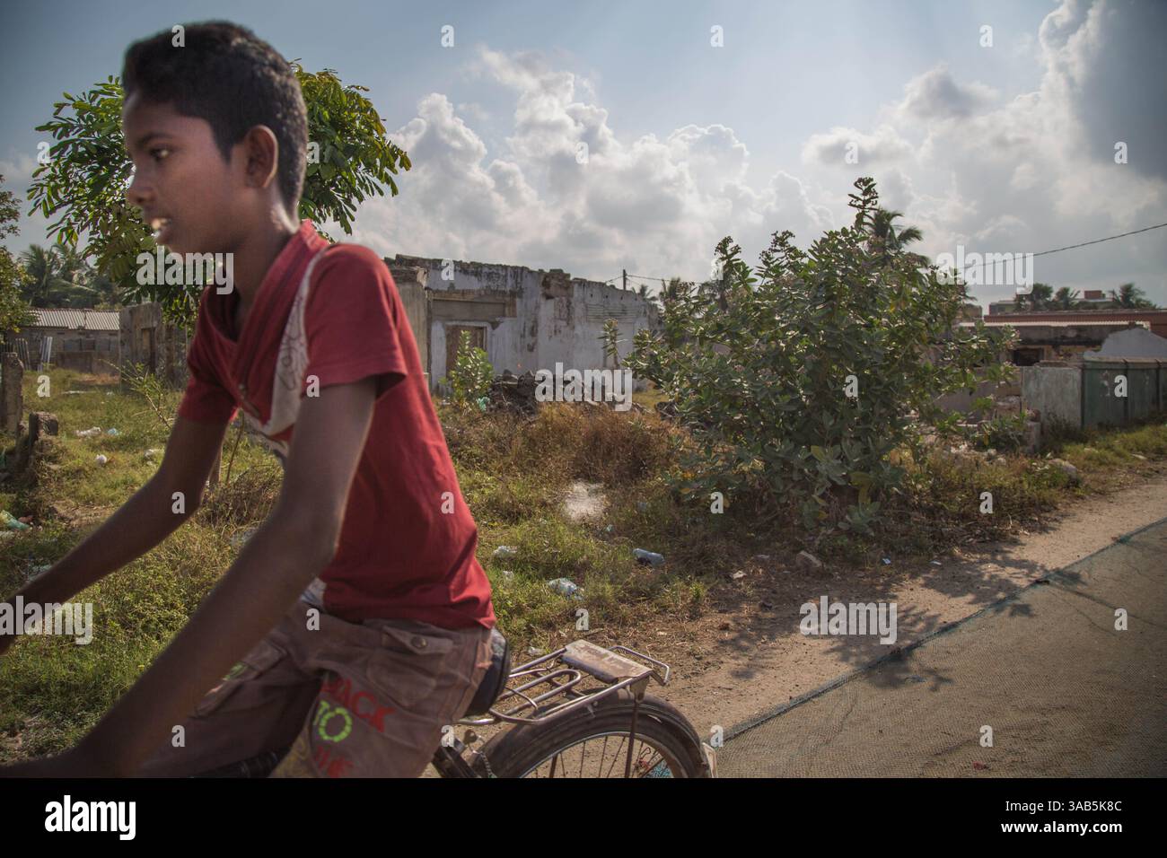 27. März 2015 – Halbinsel Jaffna, Sri Lanka – Ravi reitet an Häusern vorbei, die während des Konflikts in einem anderen Bezirk von Jaffna zerstört wurden. Er wird aus Vasavilan East vertrieben, die meisten tamilischen Jobs sind an die Orte gebunden, aus denen sie kommen. Der Sri-lankische Bürgerkrieg begann am 23. Juli 1983 und war ein Aufstand gegen die Regierung der Liberation Tigers of Tamil Eelam (LTTE oder Tamil Tigers), die für einen unabhängigen tamilischen Staat Tamil Eelam kämpften. Nach einem 26-jährigen Krieg und schätzungsweise 40.000 zivilen Toten besiegte die srilankische Armee am 2009. Mai die Tamil Tigers. Viele Tamilen waren di Stockfoto