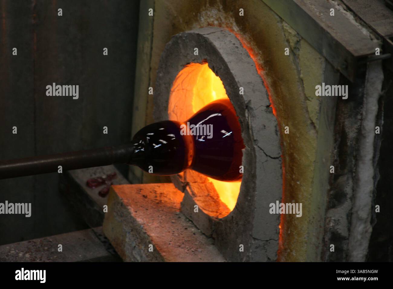 Ein Handwerker erhitzt mundgeblasenes Glas in einem Ofen, um eine wunderschöne Vase herzustellen. Stockfoto