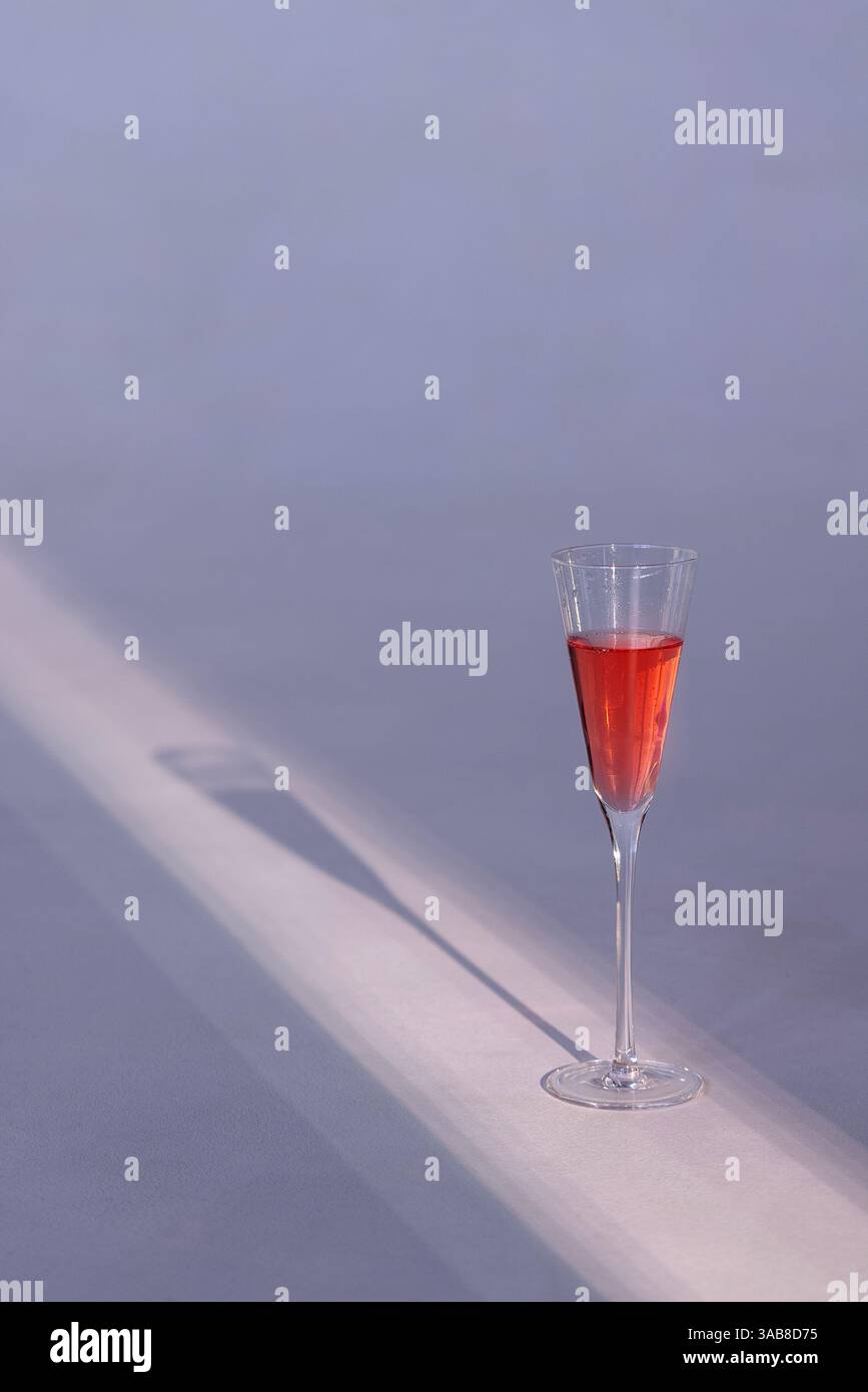 Nahaufnahme eines eleganten Glases köstlichen Champagners auf minimalistischem weißem Hintergrund. Eine Tasse leckeren rosafarbenen Sekt. Sonnenreflexe und lange SHA Stockfoto
