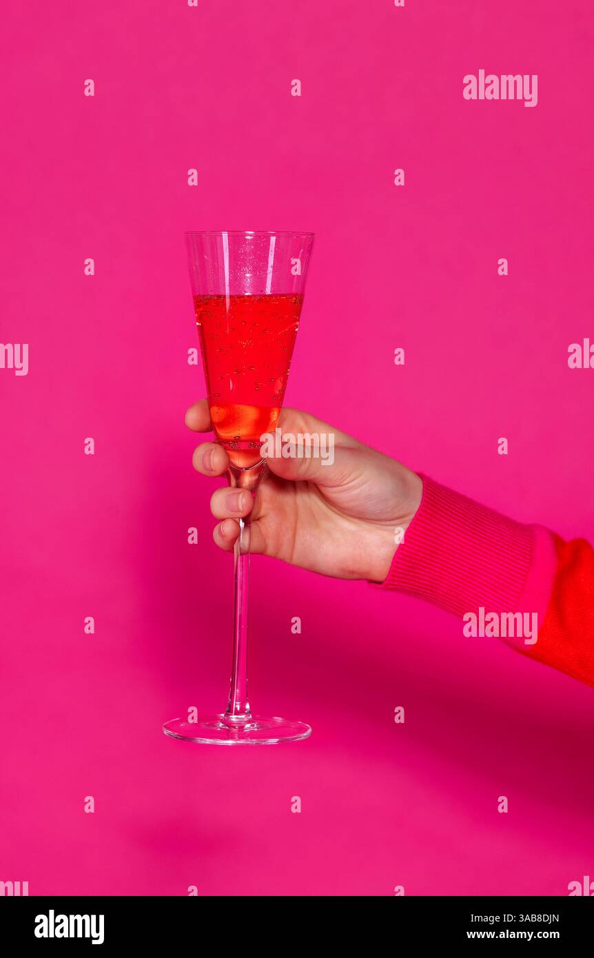 Eine weibliche Hand mit einem eleganten Glas Champagner auf einem hellen Hintergrund. Eine Frau hält einen Becher mit rosafarbenem Sekt vor einem hellen Hintergrund. Traubenalk Stockfoto