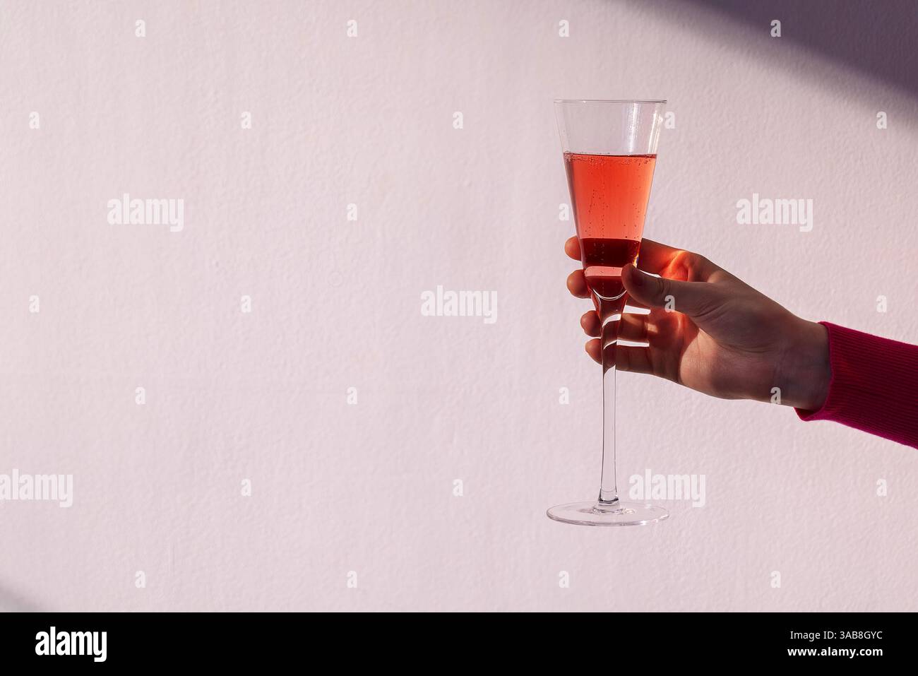 Eine weibliche Hand mit einem eleganten Glas Champagner auf weißem, strukturiertem Hintergrund. Eine Frau hält einen Becher mit rosafarbenem Sekt. Weintrauben-alkoholisch lecker Stockfoto