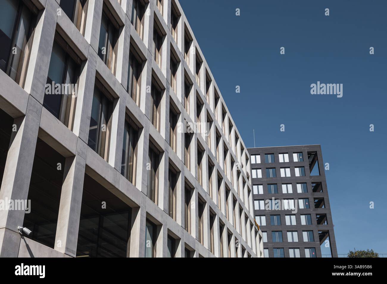 Ein perspektivischer Blick auf moderne städtische Bürogebäude mit geometrischen Designs vor klarem blauem Himmel. Architektonische Details heben Symmetrie und Fortsetzung hervor Stockfoto