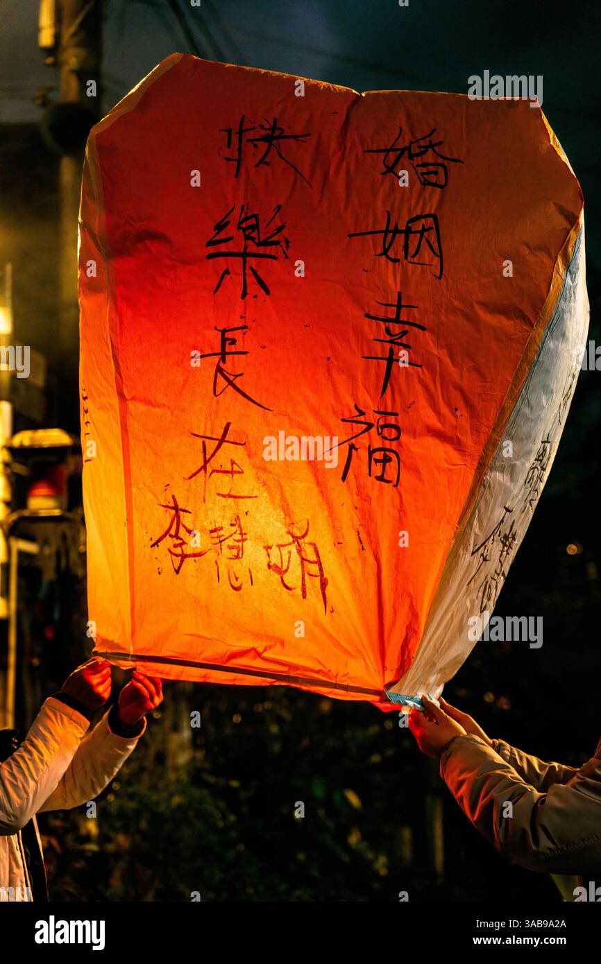 Eine lebendige, warm leuchtende chinesische schwimmende Laterne mit handgeschriebenen chinesischen Schriftzeichen, die Wünsche nach Gesundheit, Glück und Wohlstand zum Ausdruck bringen. Stockfoto