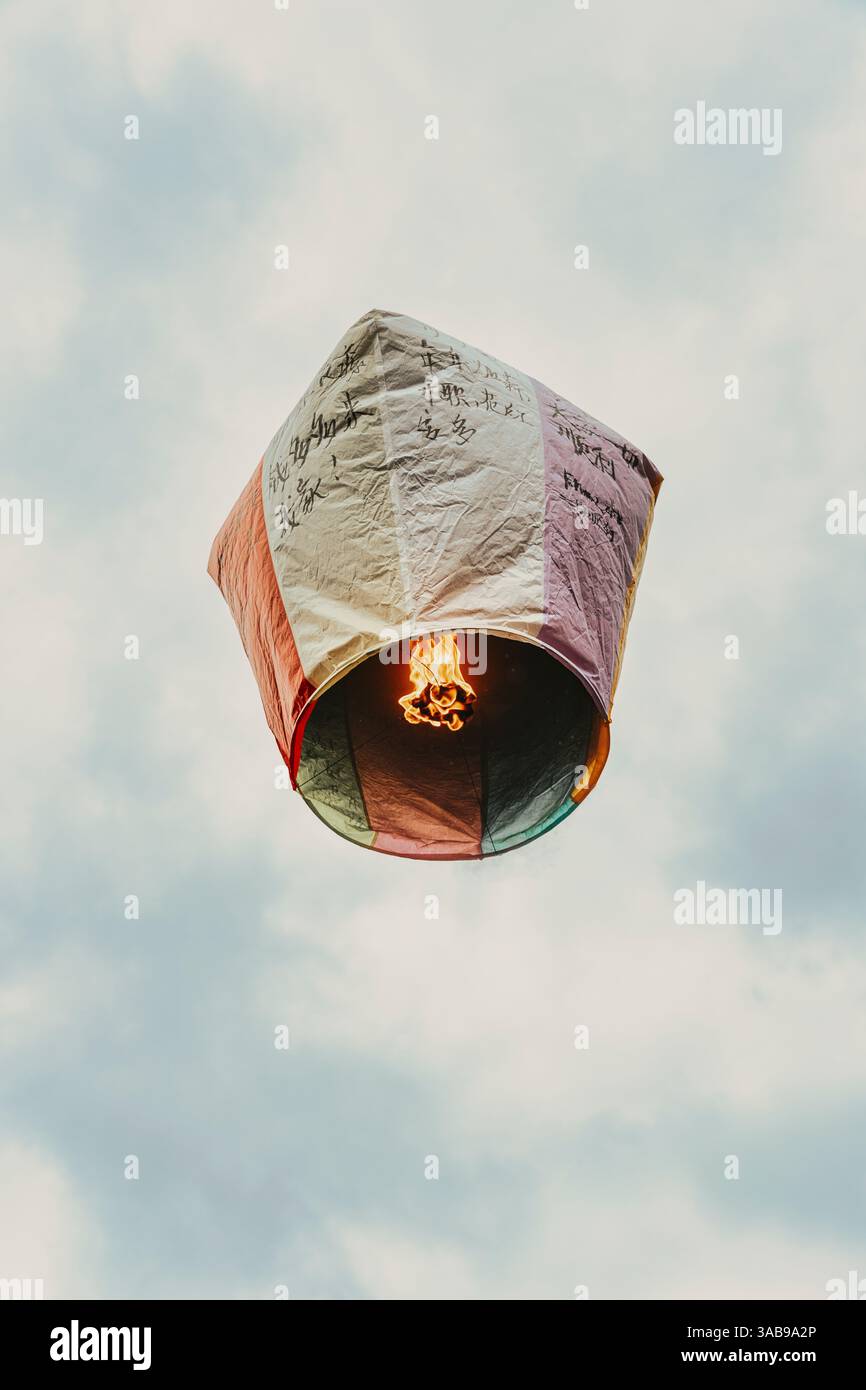 Von unten schwebt chinesische Papierlaterne in Taiwan vor einem bewölkten Himmel, geschmückt mit handgeschriebenen traditionellen Segnungen für Gesundheit, Glück und Profis Stockfoto