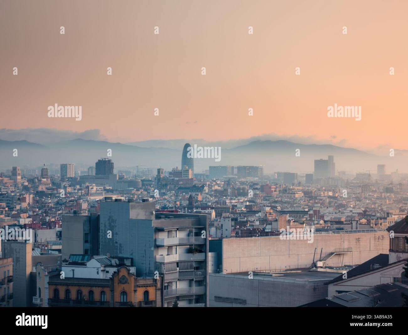 Ruhiger Blick auf Barcelona bei Sonnenaufgang, zeigt die Stadtlandschaft mit berühmten Wahrzeichen unter einem weichen, leuchtenden Himmel, mit nebelbedeckten Bergen im bac Stockfoto