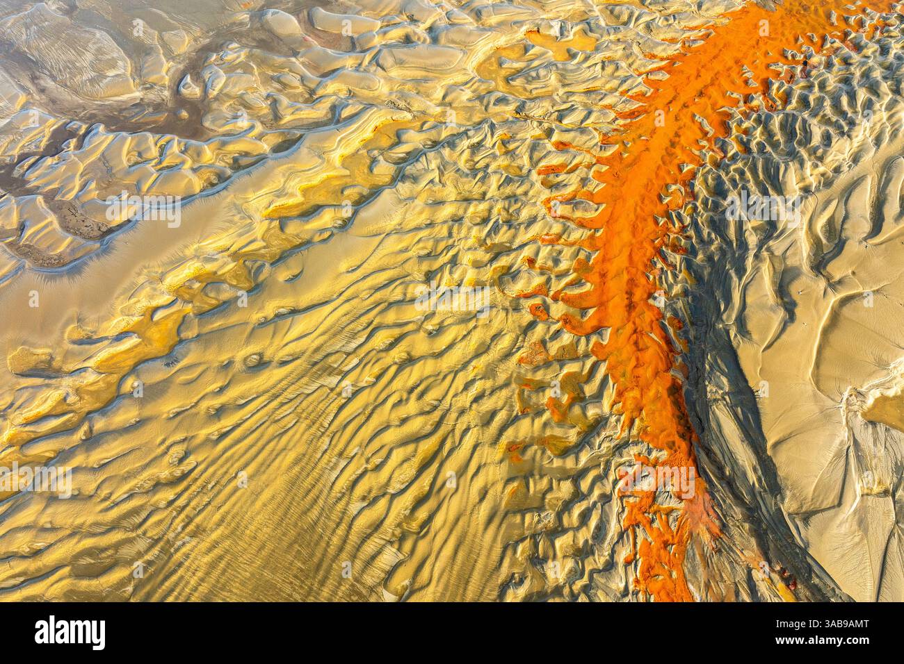 Luftbild mit markanten orangen und gelben Sandmustern, die an Wellen an einem Strand erinnern und eine faszinierende natürliche abstrakte Kunst schaffen. Ideal für B Stockfoto