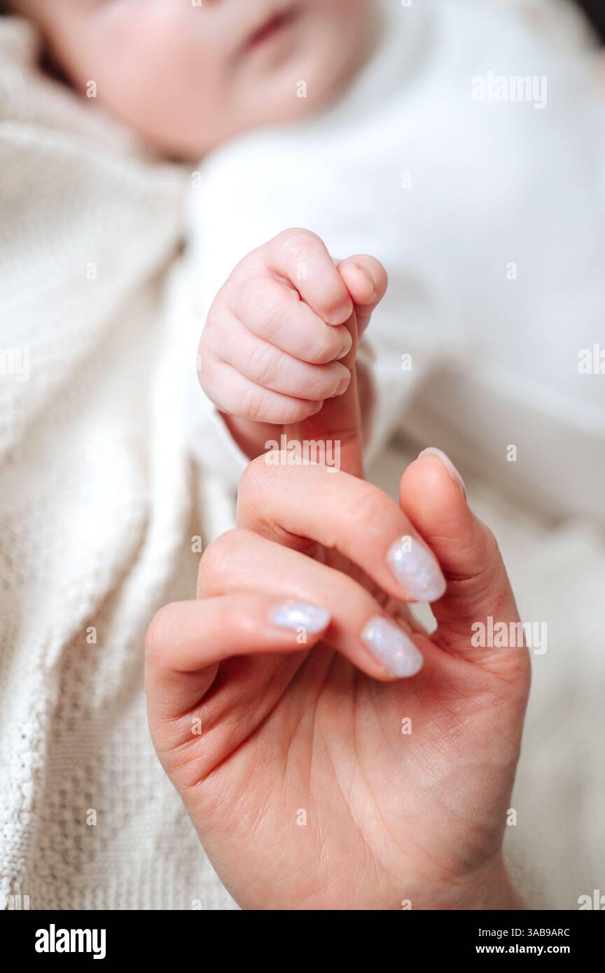 Ein Nahaufnahme-Bild, das einen zärtlichen Moment festmacht, während eine Mutter sanft die winzige Hand ihres neugeborenen Mädchens hält. Das Bild weckt Wärme, Liebe und Bindung Stockfoto