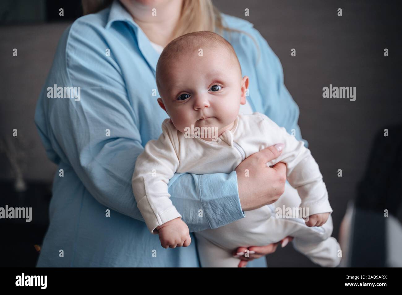 Ein süßer Junge blickt neugierig, während er von seiner Mutter sanft gehalten wird. Die intime Atmosphäre vermittelt Wärme und Zärtlichkeit und unterstreicht die Verbundenheit Stockfoto