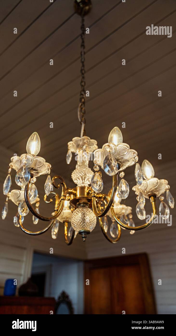 Ein luxuriöser Vintage-Kronleuchter hängt in einem gemütlichen Café mit einem warmen, einladenden Ambiente. Die goldene Befestigung und die Kristallakzente sorgen für einen Klassiker und einen eleganten Look Stockfoto
