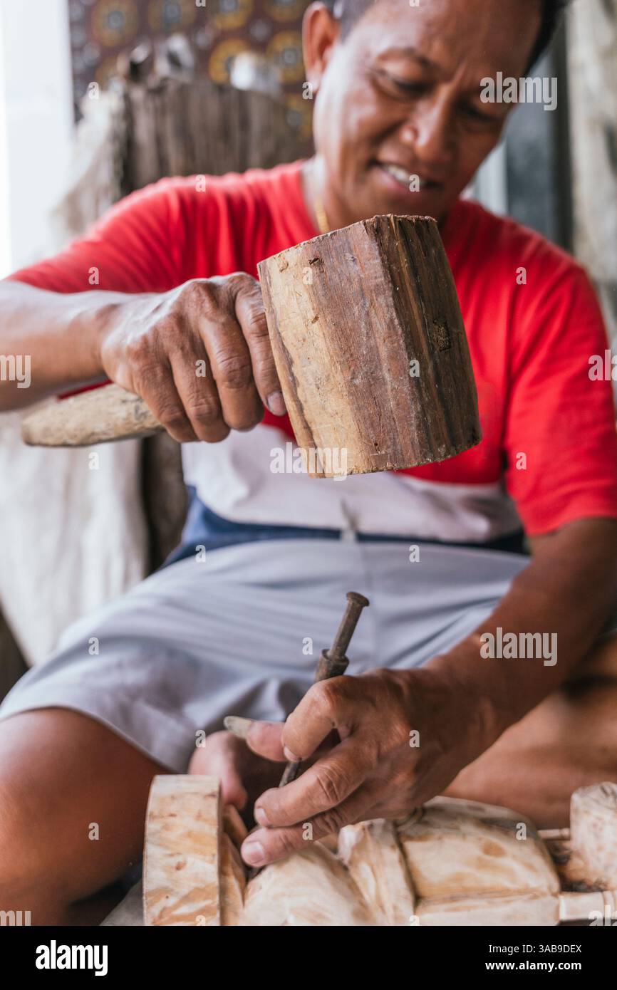 Ein indonesischer Mann schnitzt geschickt eine Holzskulptur mit traditionellen Werkzeugen und hebt die ethnische Kunst hervor. Seine Konzentration und sein Talent sind offensichtlich Stockfoto