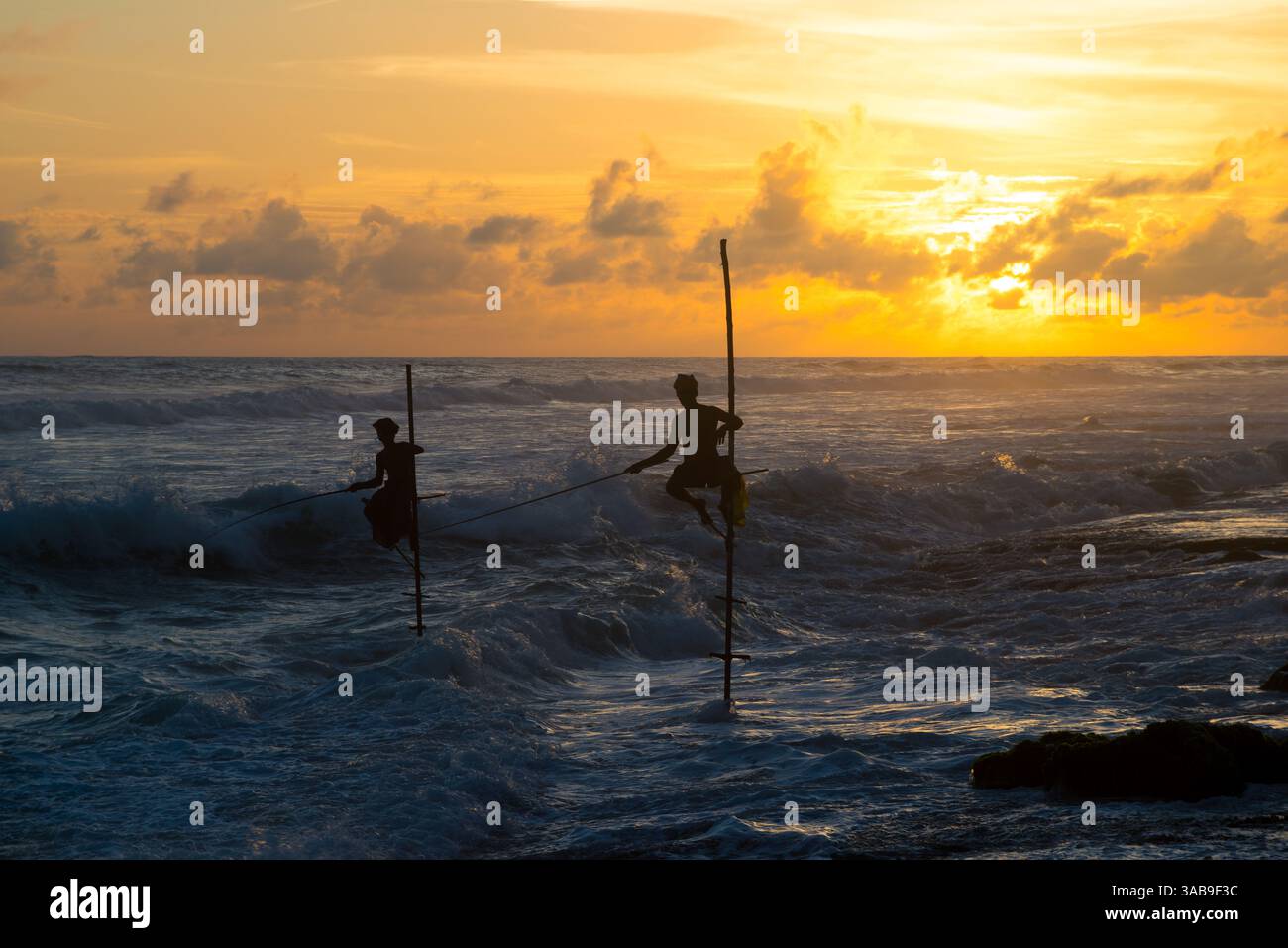 Silhouetten-Stelzenfischer üben ihr traditionelles Handwerk vor dem Hintergrund eines atemberaubenden Sonnenaufgangs über dem Meer in Sri Lanka aus und fangen ein s ein Stockfoto