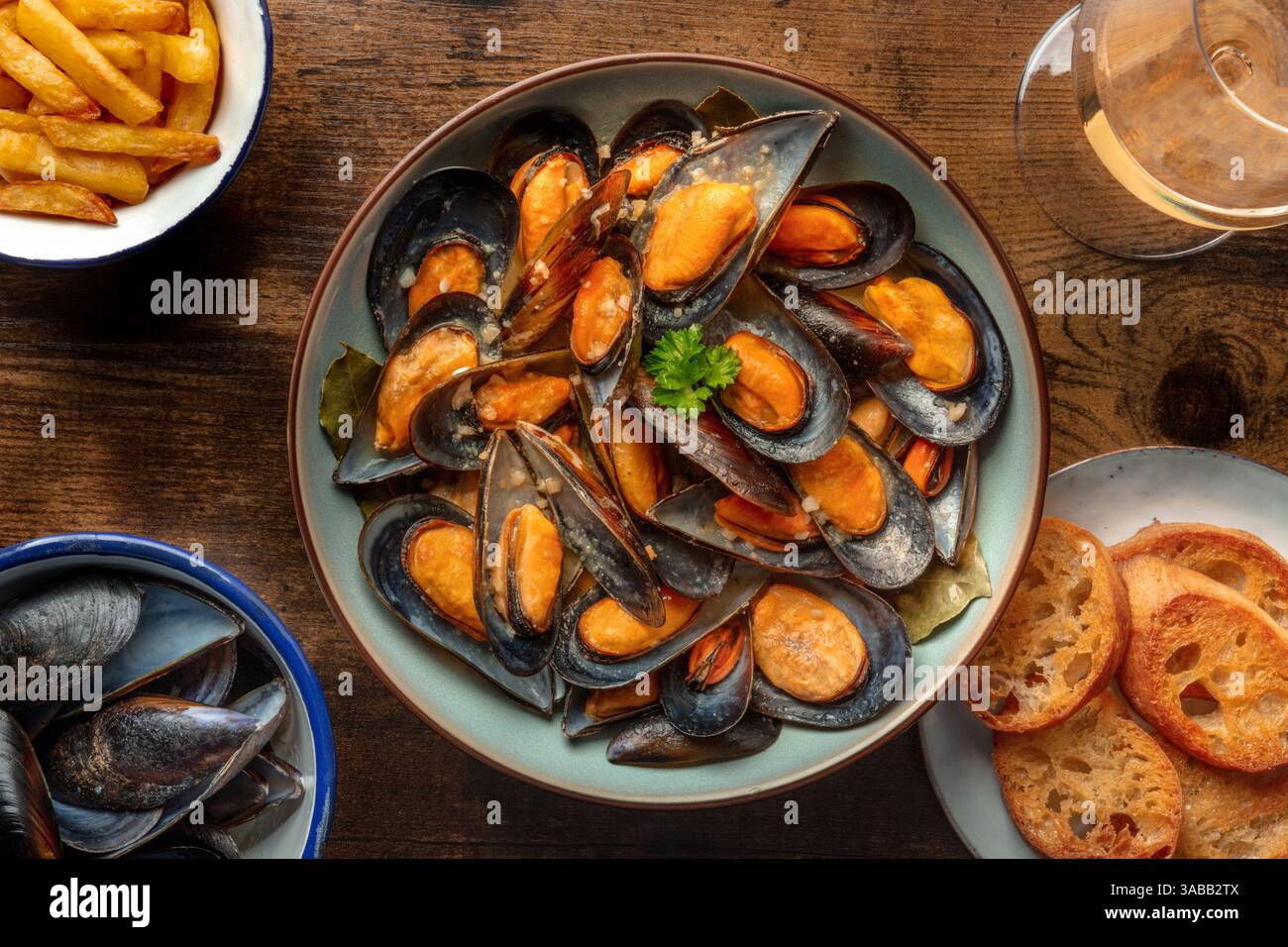 Muscheln mit Pommes frites, Weißwein und geröstetem Brot, Moules Frites, Kopfschuss auf einem Holztisch Stockfoto