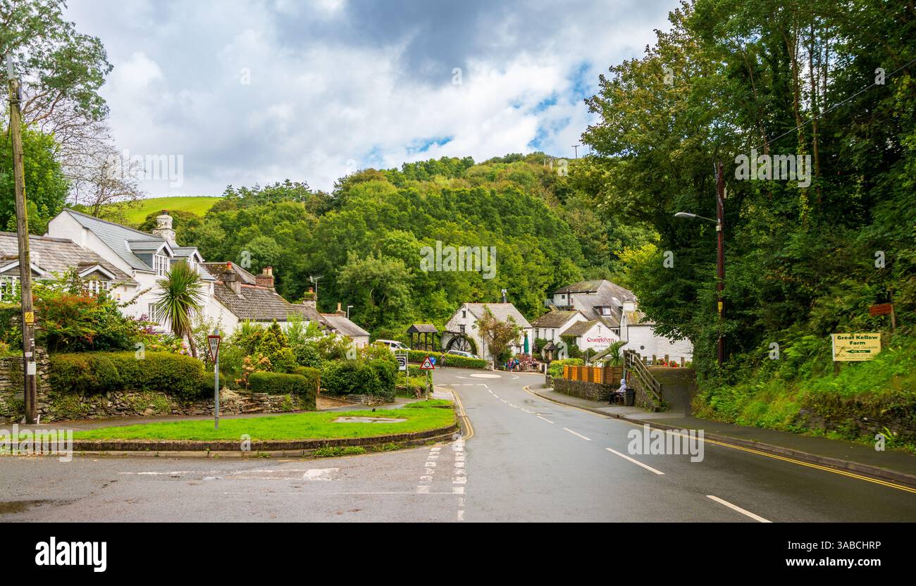 Die bezaubernde Straße von Polperro führt durch üppiges Grün und traditionelle Häuser unter einem bewölkten Himmel. Stockfoto
