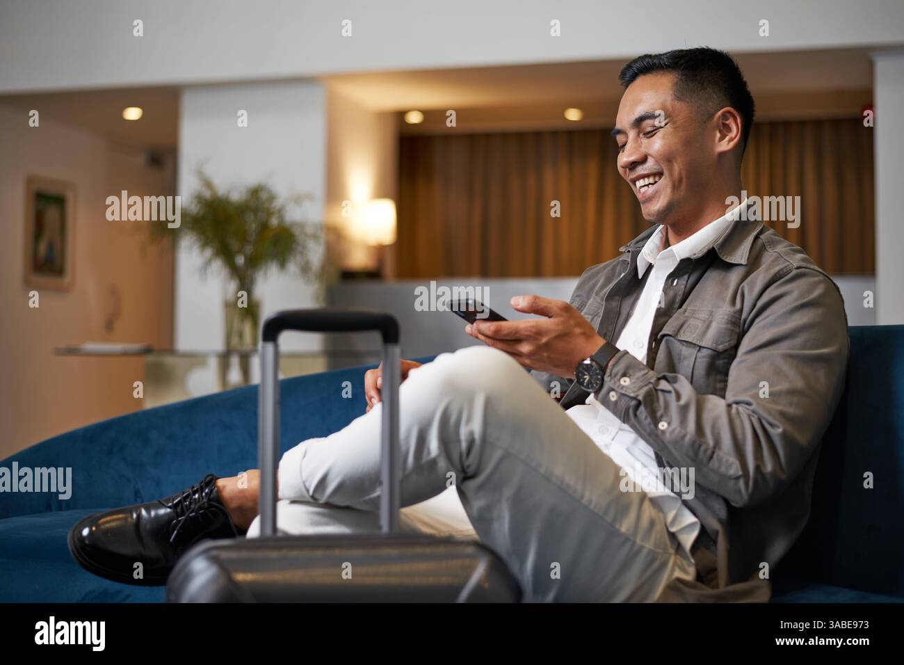 Entspannter Geschäftsreisender in der Hotellobby, der während der Wartezeit das Smartphone überprüft Stockfoto