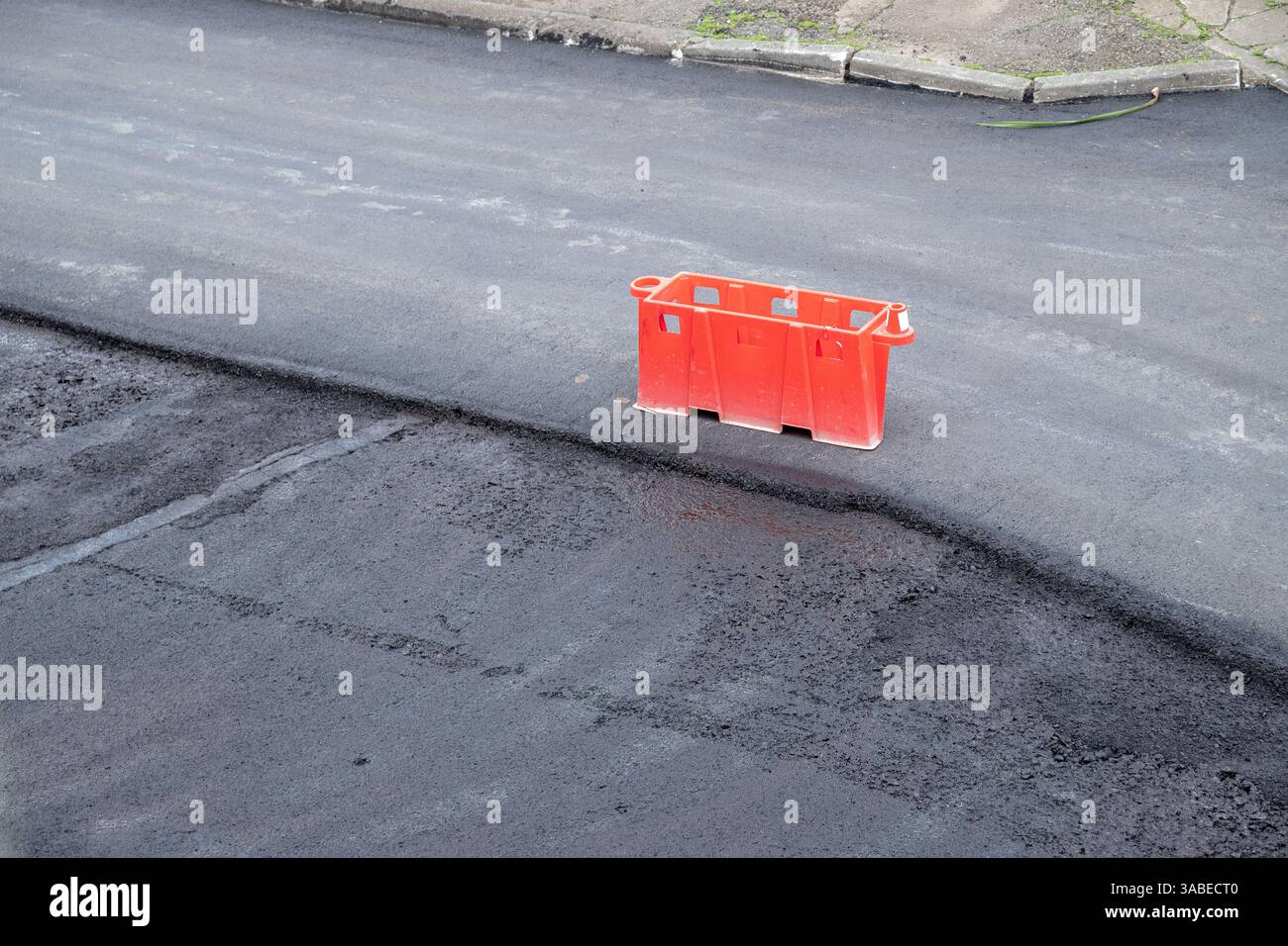 Neu gepflasterte öffentliche Straße wird gewartet, mit frischer Asphaltschicht. Orangefarbene Barrieren markieren Sperrbereiche aus Sicherheitsgründen. Stockfoto