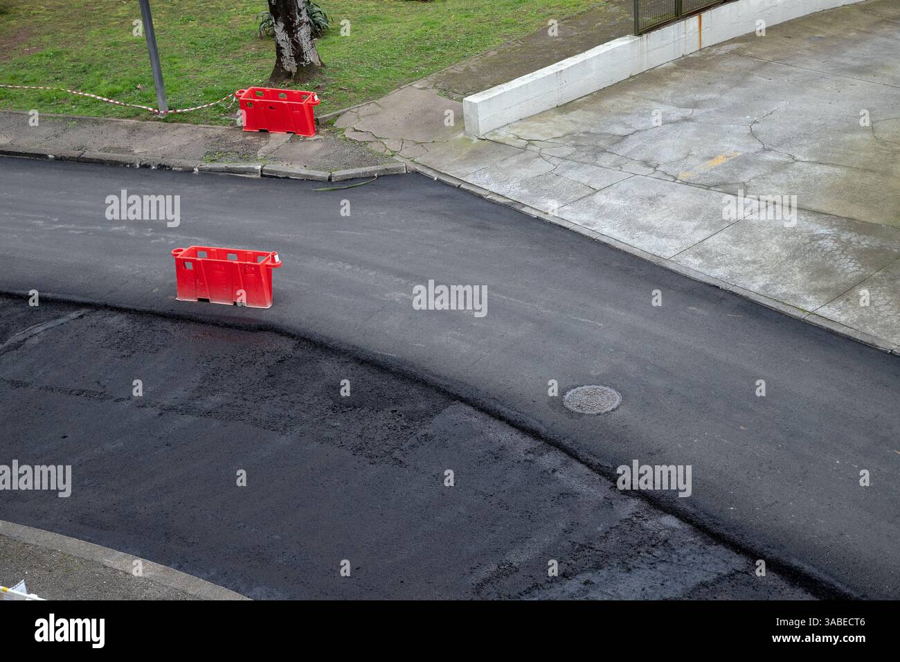 Neu gepflasterte öffentliche Straße wird gewartet, mit frischer Asphaltschicht. Orangefarbene Barrieren markieren Sperrbereiche aus Sicherheitsgründen. Stockfoto