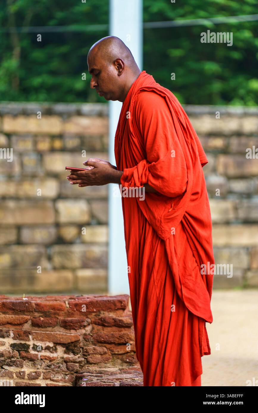 Ein buddhistischer Mönch in einem traditionellen roten Gewand betet mit Hingabe an einer antiken Stätte in Polonnaruwa, Sri Lanka, und verkörpert Spiritualität und friedliche Umgebung Stockfoto