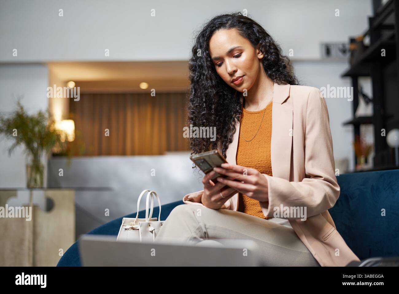Selbstbewusste professionelle Frau, die in der Hotellobby sitzt und ihr Telefon überprüft Stockfoto