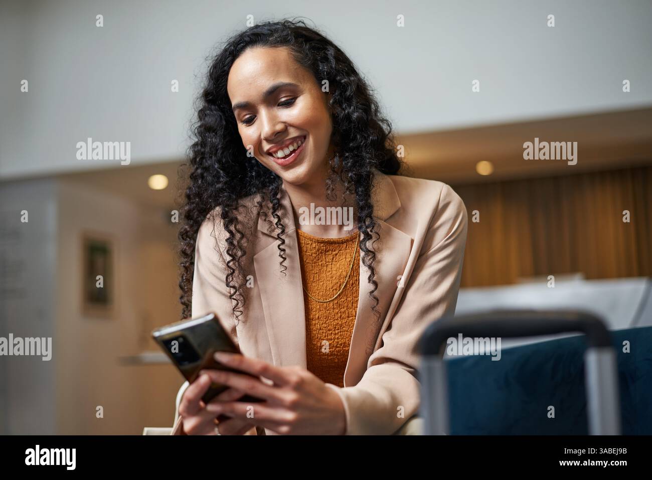 Lächelnde Geschäftsfrau mit Smartphone in moderner Hotellobby Stockfoto