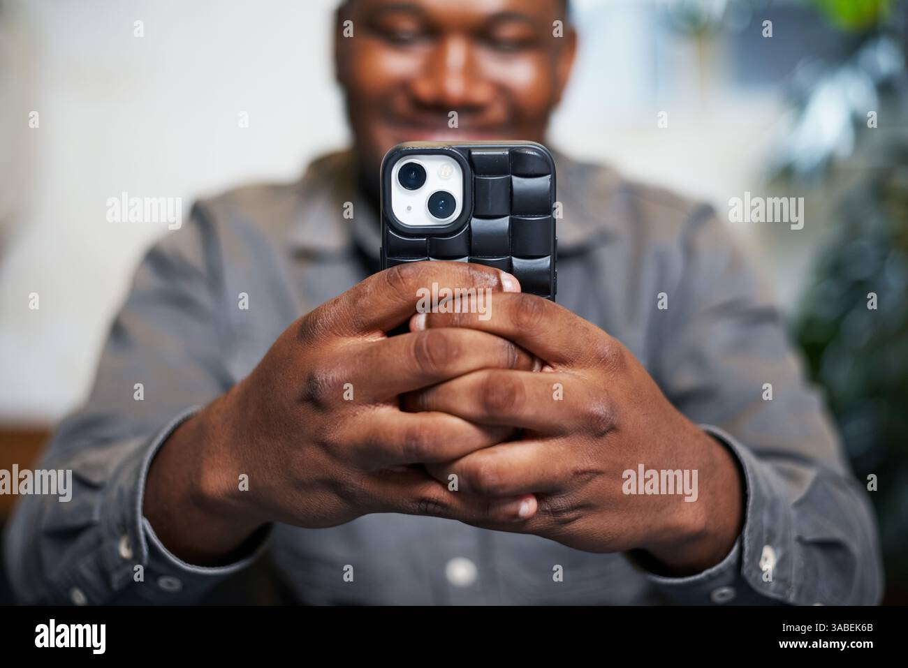 Mann hält Smartphone mit stilvoller Hülle und lächelnd in einer modernen hellen Umgebung Stockfoto
