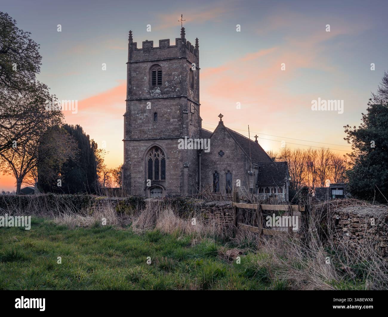 Long Newnton, Gloucestershire – die Sonne geht hinter der Holy Trinity Church in Long Newnton auf, einem kleinen Dorf und einer Zivilpfarrei in Gloucestershire, Clo Stockfoto