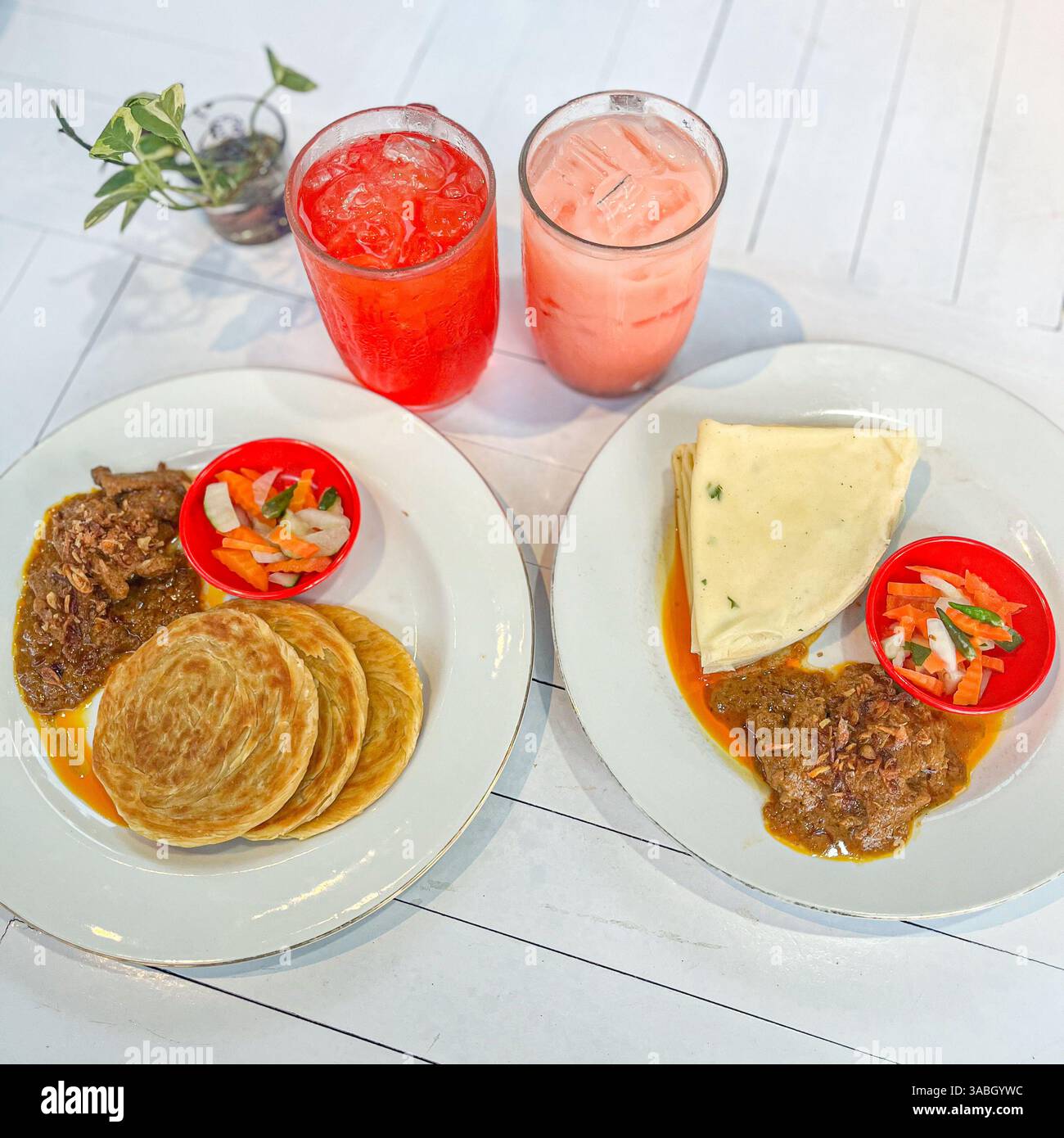 roti Prata, oder Roti Canai serviert mit Rindfleisch Rendang, Gurken und frischem Saft auf weißem Hintergrund - Smartphone-aufgenommenes Stockfoto