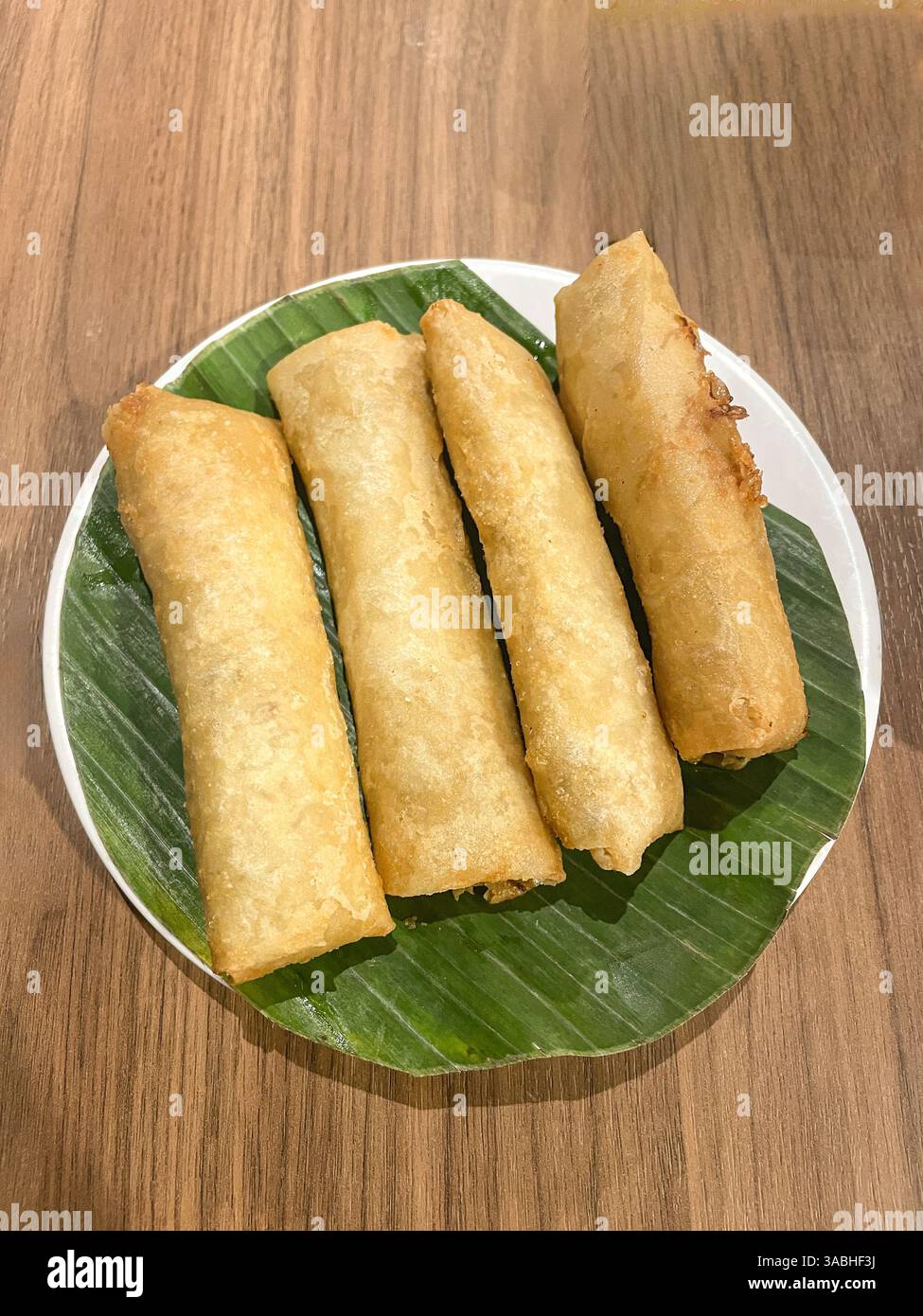 Frittierte Frühlingsrollen auf weißem Teller und Bananenblätter, Blick von oben - Smartphone-aufgenommenes Stockfoto