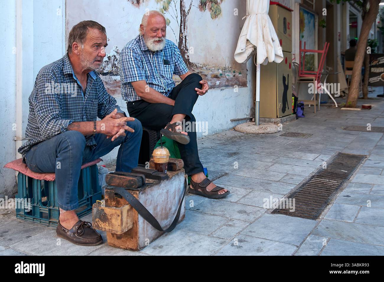 Kreta. Griechenland - 02. april 2025: Schuhputzer auf einer Kiste mit Pinseln und politur, die ein traditionelles Handwerk in einer lebhaften griechischen Stadt widerspiegelt Stockfoto