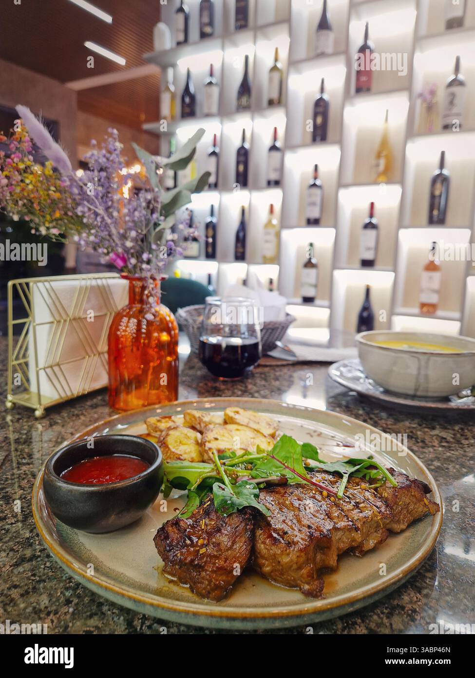 Gegrilltes Rindersteak auf dem Tisch in einem schicken Restaurant mit Blick auf die Weinregale im Hintergrund - Smartphone-aufgenommenes Stockfoto