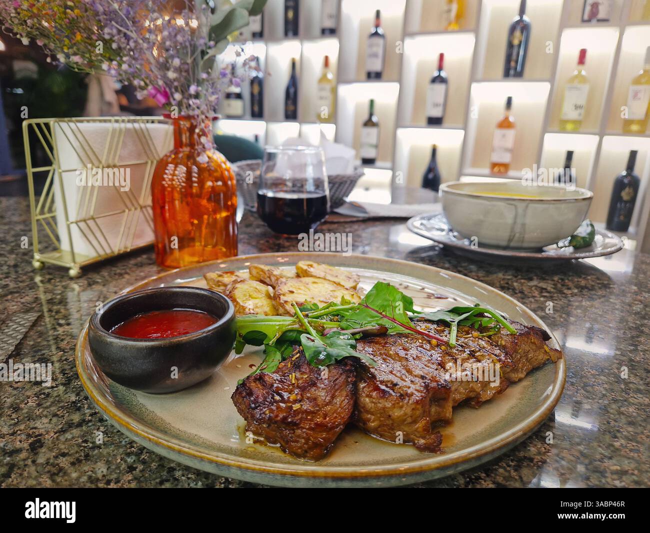 Gegrilltes Rindersteak auf dem Tisch in einem schicken Restaurant mit Blick auf die Weinregale im Hintergrund - Smartphone-aufgenommenes Stockfoto