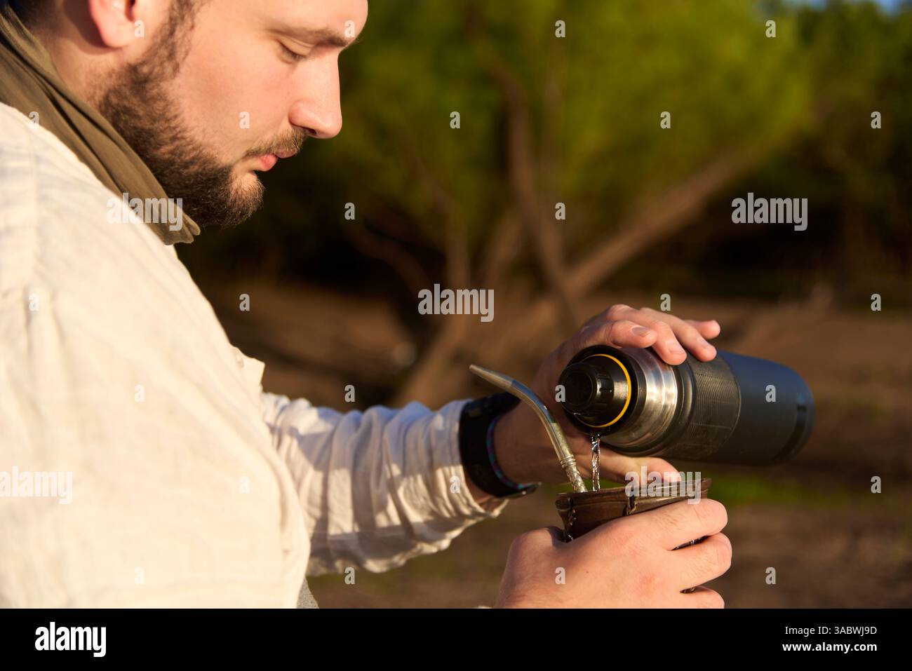 Hispanischer Mann, der Wasser aus einer Thermoskanne in einen Paare gießt, um diesen traditionellen argentinischen Aufguss zu trinken. Stockfoto