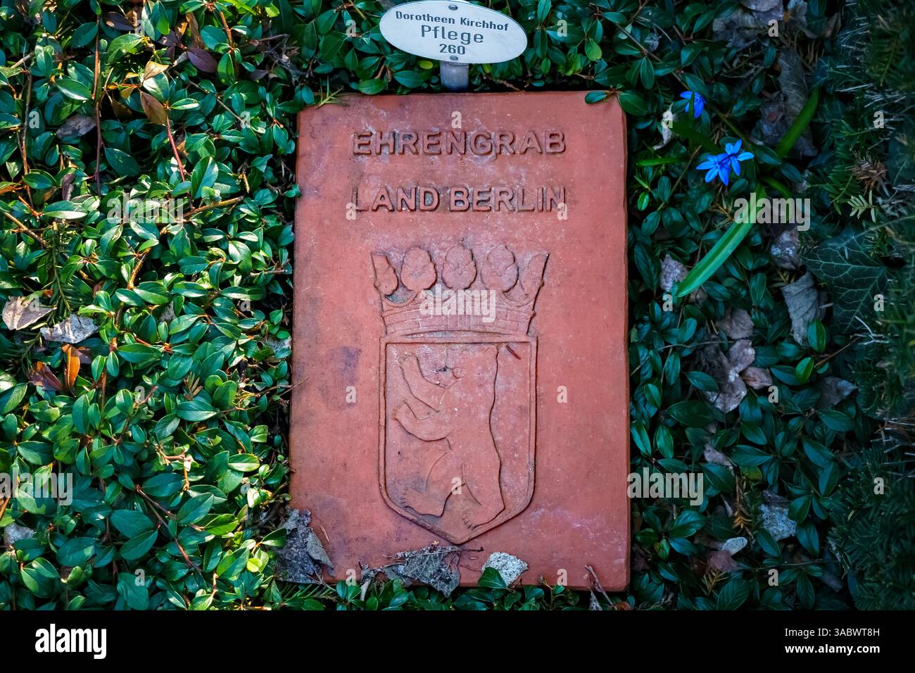 Nahaufnahme eines roten Ehrengrabmarkers mit der Aufschrift „Ehrengrab Land Berlin“ mit dem Berliner Bären-Emblem auf dem Dorotheenstadt-Friedhof in Berlin. Stockfoto