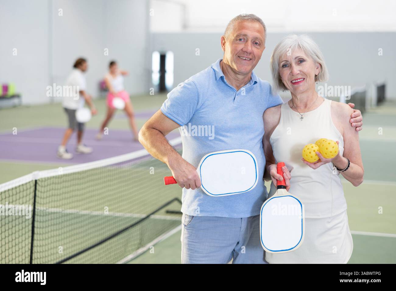 Ältere Ehepaare mit Schlägern und Bällen, die auf dem Pickleball-Platz posieren Stockfoto