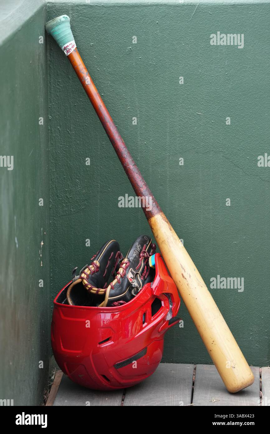 Baseballausrüstung einschließlich Schläger, Helm und Handschuh in der Ecke eines Dugouts während eines Baseballspiels. Stockfoto