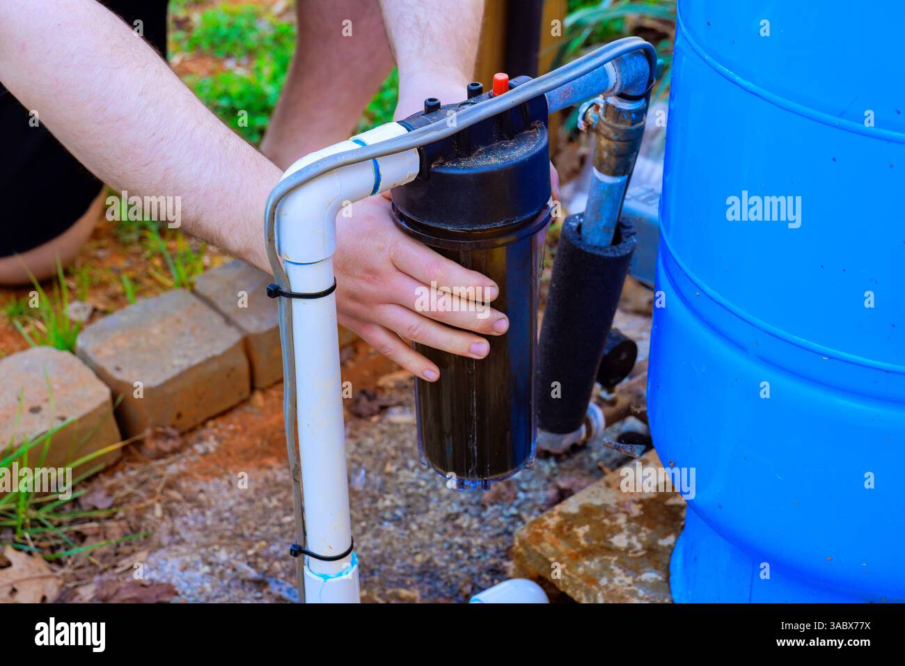 Person, die den Wasserfilter im Freien an das Regenwassersammelsystem im Garten auswechselt. Stockfoto