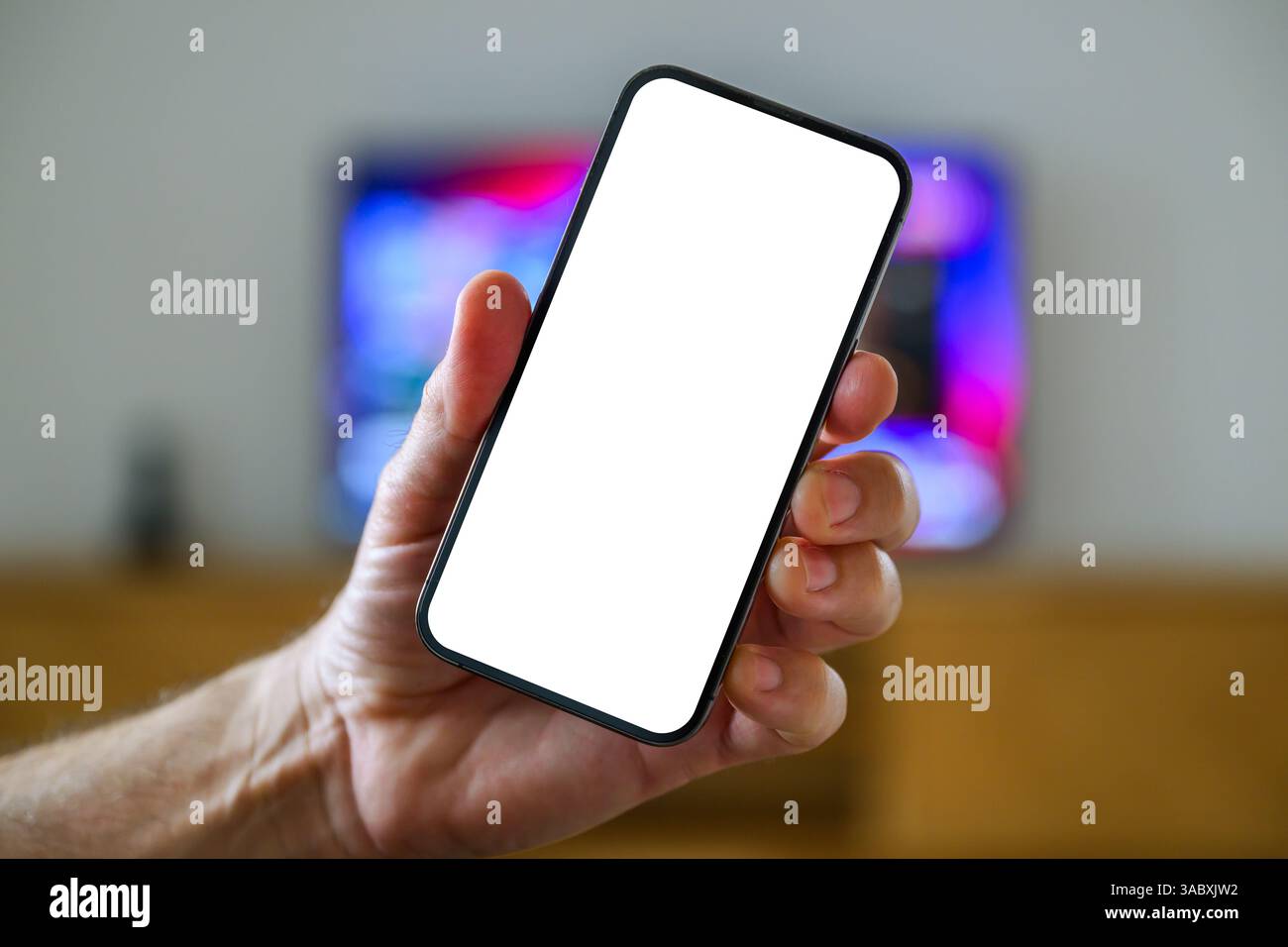 Smartphone-Mockup-Bildschirm, Mann, der das Handy vor dem Fernseher hält, tv-App und tv-Programm-Auflistung Konzept, selektiver Fokus Stockfoto