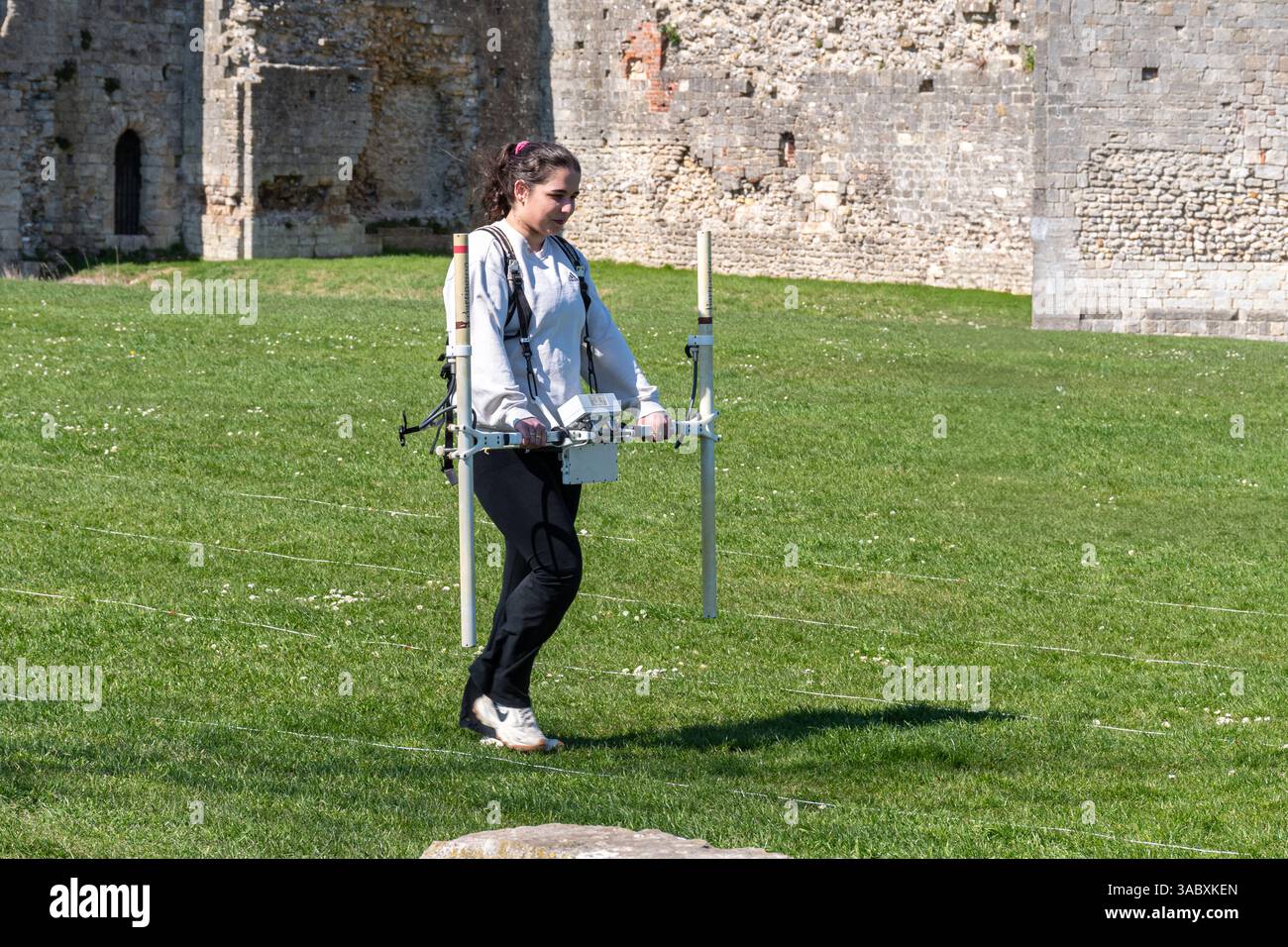 Archäologiestudent, der eine geophysikalische Untersuchung mit einem Magnetometer durchführt, Portchester Castle, Hampshire, England, Großbritannien Stockfoto