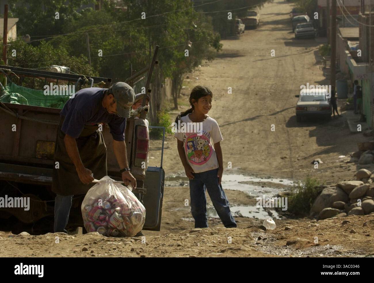 (Veröffentlicht am 9. August 2004, B-8:1,7; UTS1824435) Guadalupe Velasquez Perez, 7, schaut auf ihre Schwestern in ihrem Haus in Colonia Diez de Mayo in Tijuana, während der Schrottkäufer Ramon Olmedo die Dosen bündelt, die sie ihm zum Verkauf brachte. Sie holte sie aus der Nachbarschaft ab und wartete darauf, dass sein Truck vorbeikam, damit sie sie gegen Pesos eintauschen konnte. Olmedo bringt seine gesammelten Schrott- und Aluminiumschrott am Ende des Tages zu einer Recyclinganlage. Peggy Peattie Foto Stockfoto