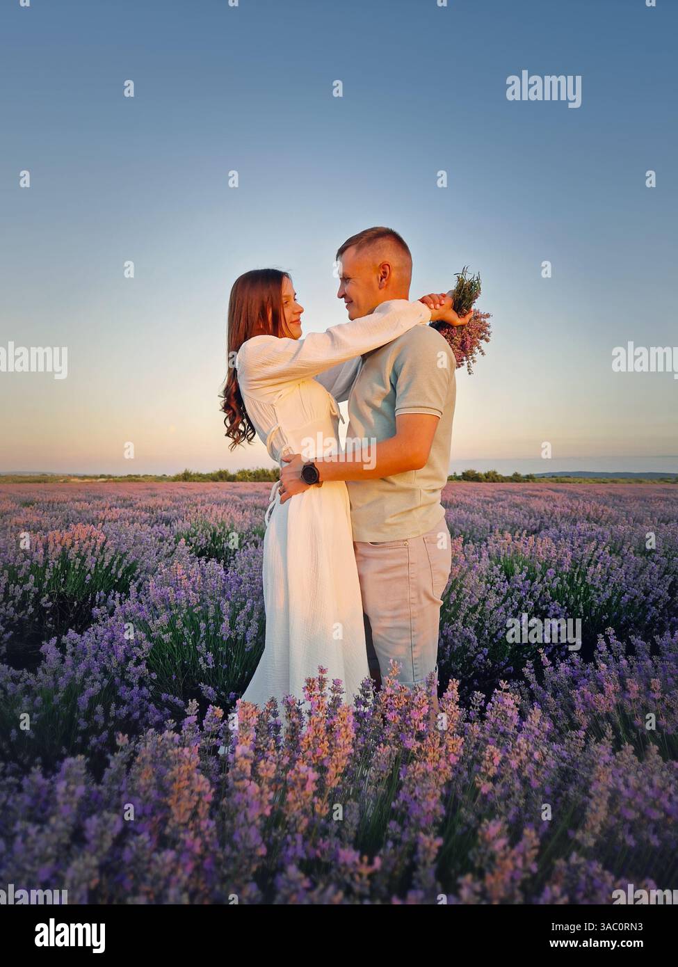 Ein Paar, das sich auf einem Date im Lavendelblumenfeld umarmt. Idyllische Sommerszene, Liebe und Romantik - Smartphone-aufgenommenes Stockfoto